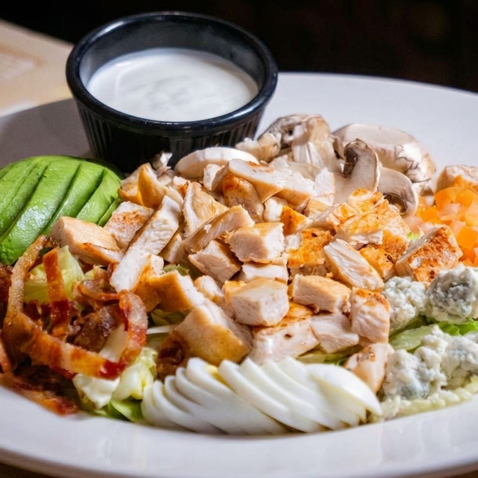 Cobb salad topped with grilled chicken, avocado, bacon, mushrooms, tomatoes, blue cheese, boiled egg, and creamy dressing.