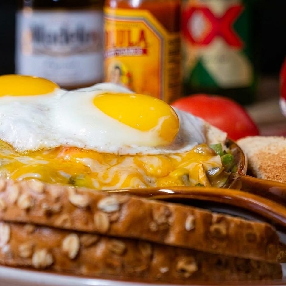 Cheesy hash browns topped with two fried eggs, served with toasted multigrain bread and condiments.